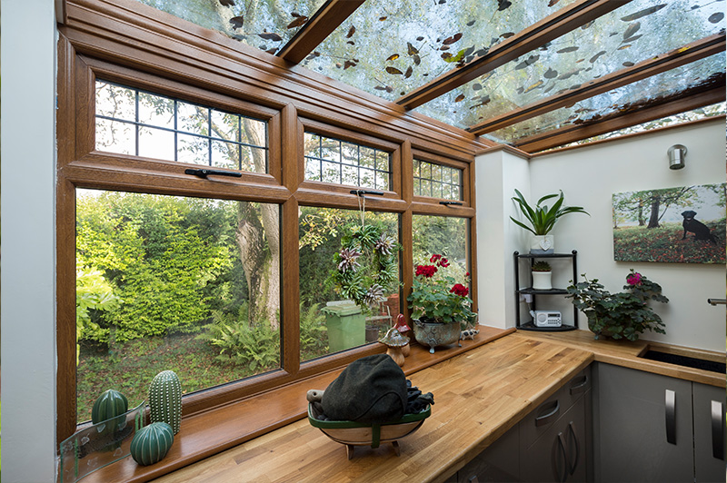 Golden oak uPVC sun-lounger conservatory used as a kitchen overlooking a garden