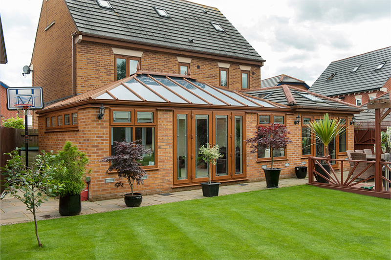 Exterior of modern house with large golden oak uPVC conservatory, glass roof, and French doors leading to the rear garden