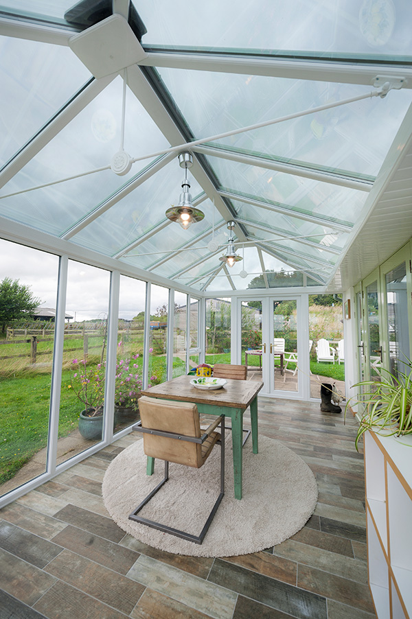 Interior view of a traditional white-framed conservatory with full-height windows, French doors, and a glass roof overlooking a country garden in Leicestershire.