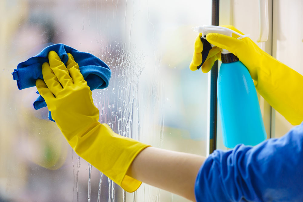 Person cleaning a uPVC window from the inside with yellow gloves in a Leicester home