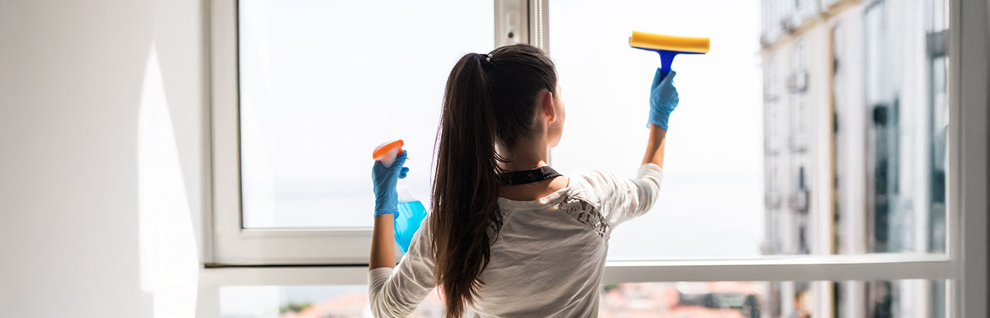 Person cleaning a uPVC window from the inside with blue gloves in a Leicester home