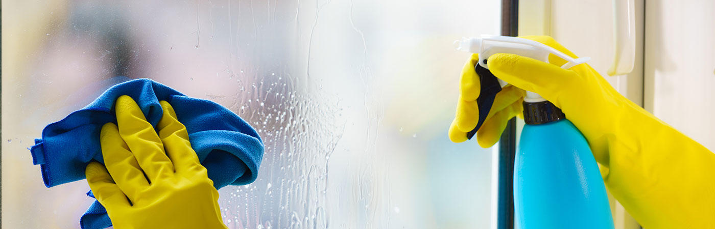 Person cleaning a uPVC window from the inside with yellow gloves in a Leicester home